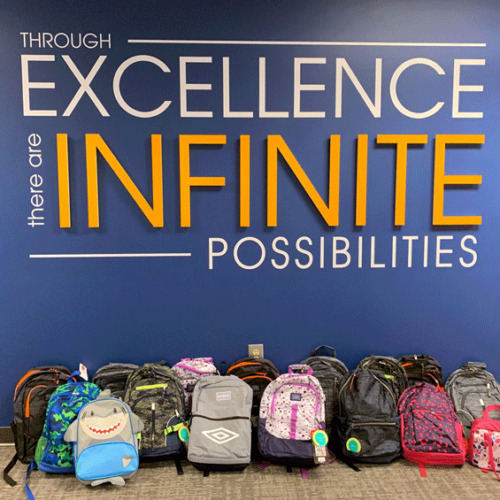 backpacks sitting on ground in front of sign that says excellence infinite possbilities